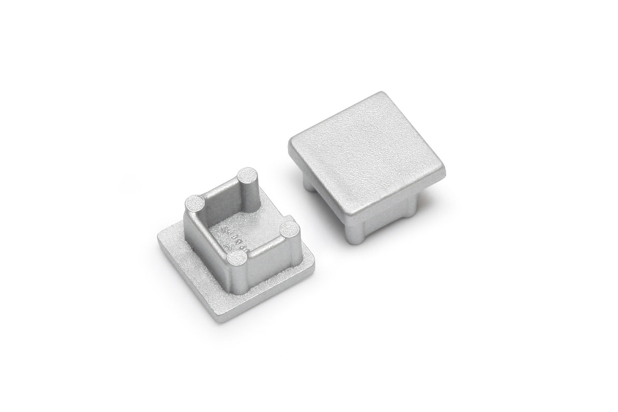 Two small, square, silver End Caps for Smart10 Profile are shown on a white background—one upright to display its smooth surface, the other flipped to reveal four inner posts. Perfect finishing touch for your lighting fixture.