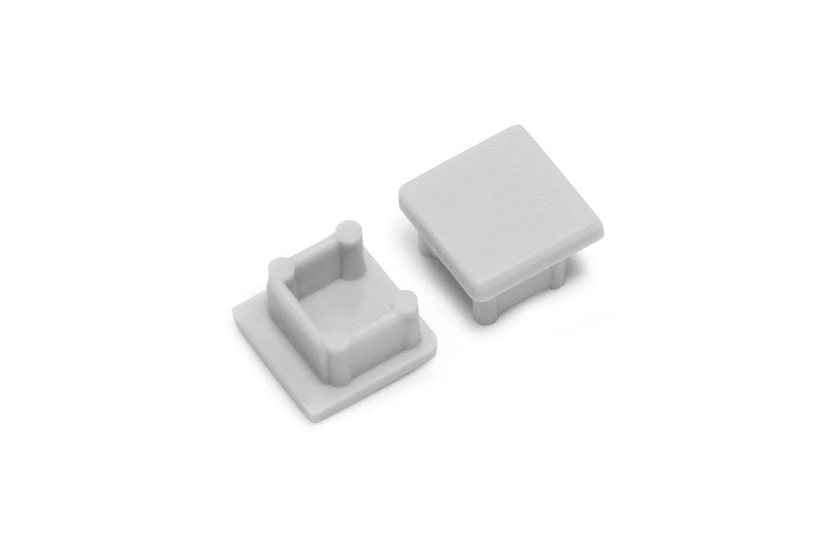 Two small, square, light gray plastic End Caps for Smart10 Profile are shown; one stands upright showing the flat top, while the other is flipped to reveal four inner pegs for secure attachment to the lighting fixture.