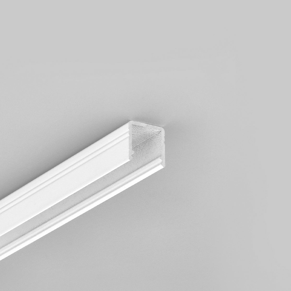 The Miniature Surface Mount LED Channel ~ Model Smart10 is shown in white aluminum with a U-shaped profile against a light gray background, angled to highlight its shape and length—ideal for modern interior lighting applications.