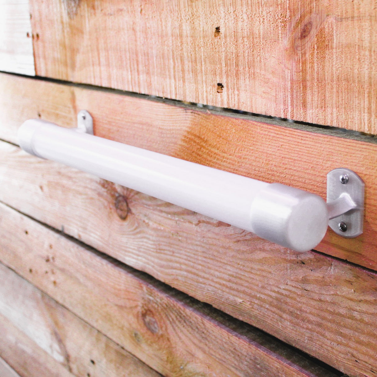 The Wired Post for 1.50 Round Profiles is a cylindrical LED wall light with brass or stainless steel ends, mounted horizontally on wood and featuring diffuser tubes for even illumination.