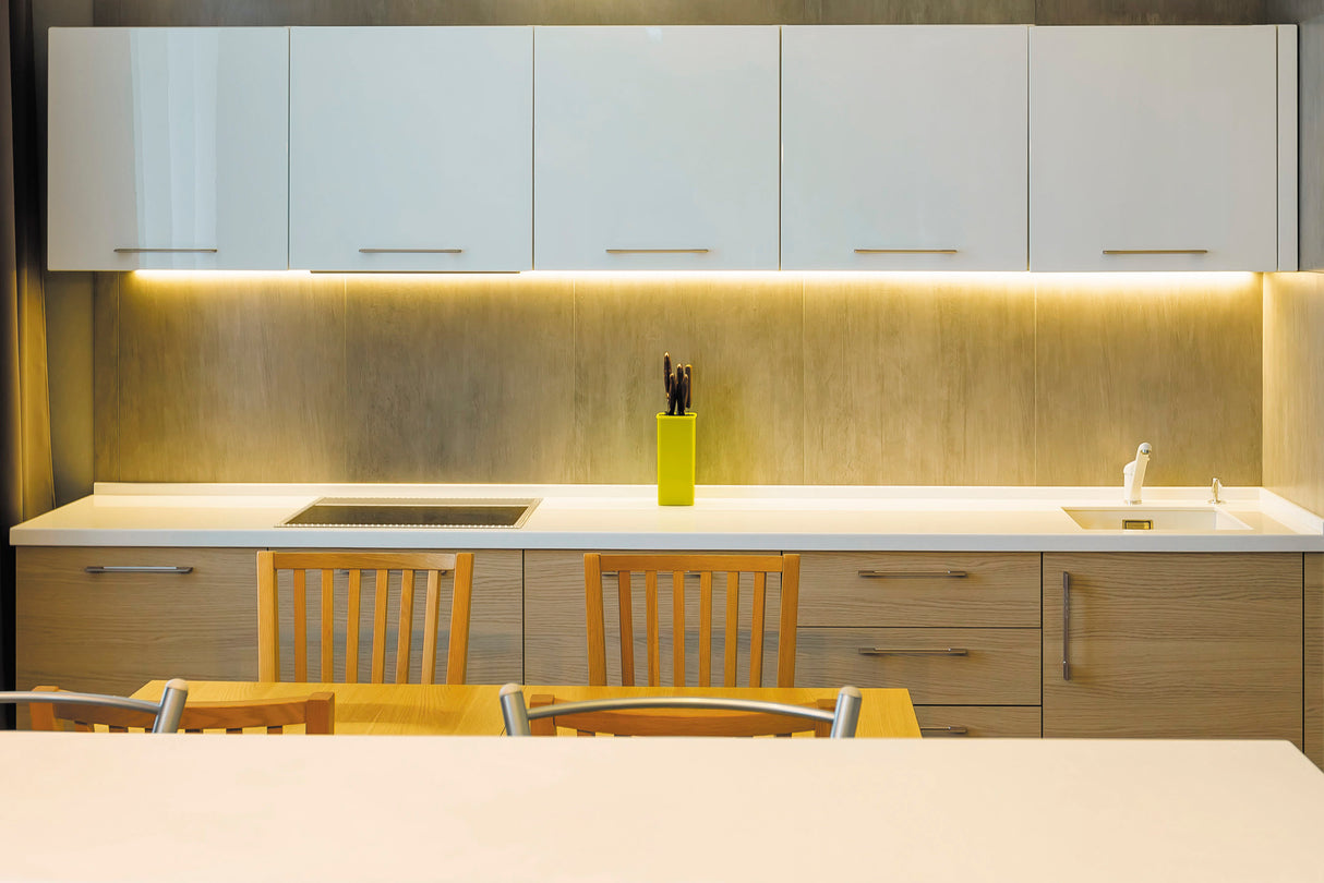 Modern kitchen with light wood cabinets, built-in stovetop, and white countertop. The 35/55 Degree Corner LED Lighting Channel ~ Model Texas Mini provides a warm under-cabinet glow, highlighting the sink and contemporary decor.