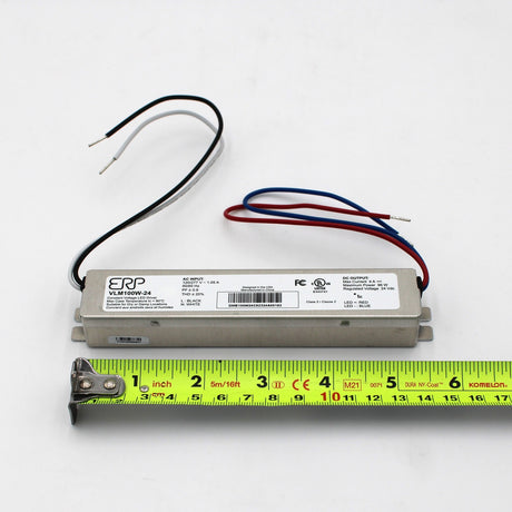 The Slimline Small Constant Voltage LED Driver (24V) from the ERP Power VLM Series is a compact, rectangular power supply with red, blue, black, and white wires pictured on a white surface beside a yellow tape measure showing its 16 cm length.