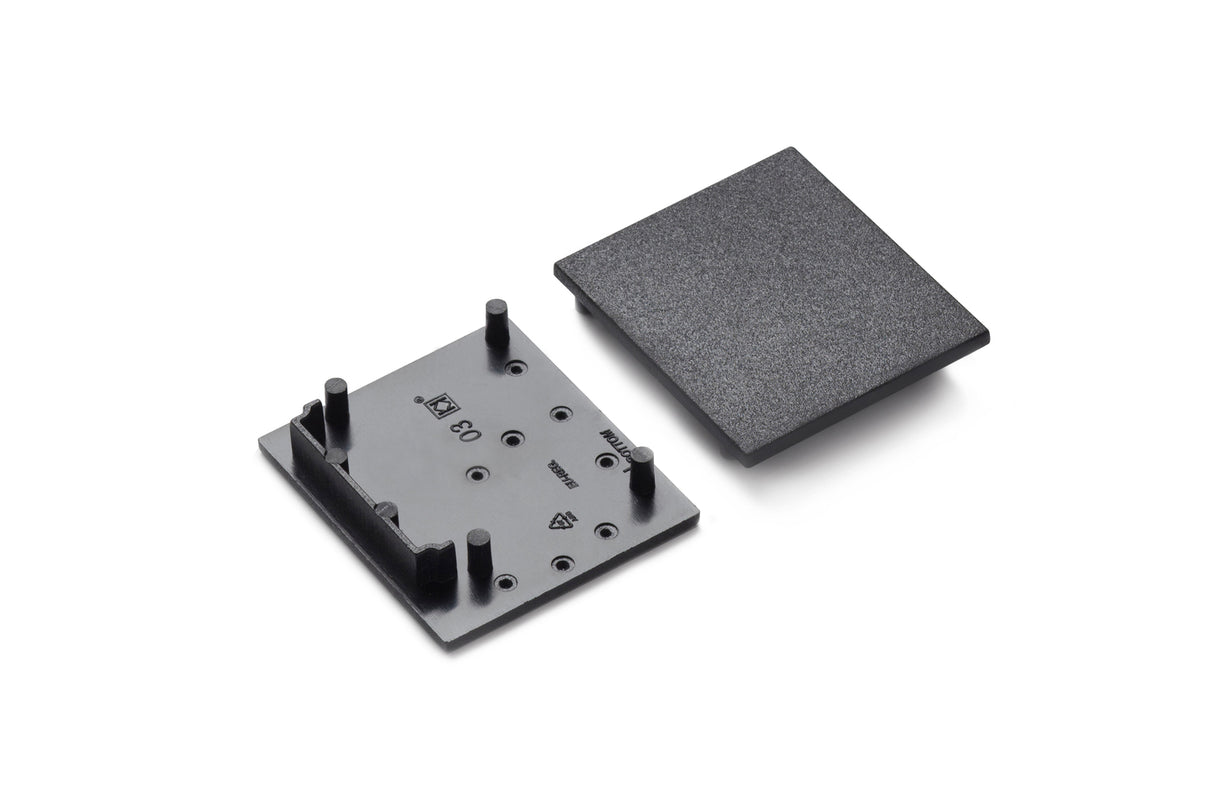 Two black plastic parts—a textured end cap and a flat base with four pegs—are shown for the End Cap for Vario30-03 Profile lighting fixture, featuring several small markings or symbols on their surfaces.