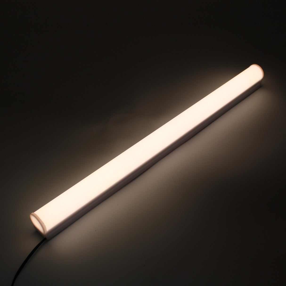 The White Border Contour Tube Light ~ Hi-Lite 30 Straight Section emits a soft white glow against a dark backdrop. Positioned diagonally, it features a power cord on one end and is securely mounted with polycarbonate clips—perfect for building illumination.