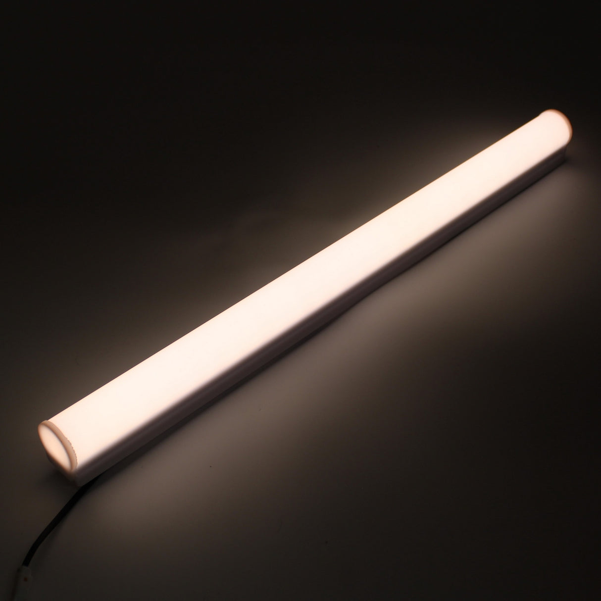 A White Border Contour Tube Light ~ Hi-Lite 30 Field Adjustable is positioned diagonally on a dark surface, casting a soft, even glow perfect for building illumination. A black wire extends from the end of the tube.