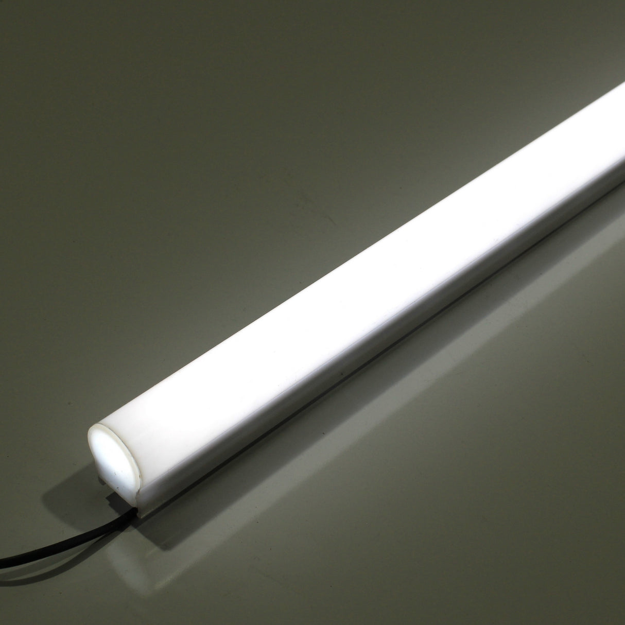 A White Border Contour Tube Light ~ Hi-Lite 30 Field Adjustable glows diagonally on a smooth, reflective surface with a black power cord—ideal for modern building illumination.