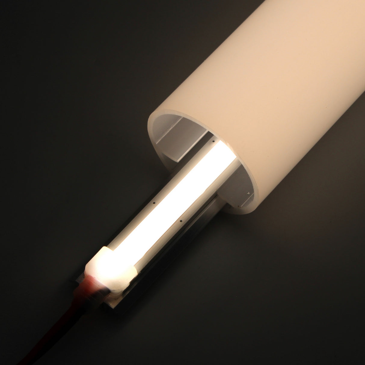 A close-up of the Flat Bar Aluminum Heatsink LED Profile ~ Model Yukon shows its modern white cylindrical form with a glowing LED tube and integrated aluminum heatsink for heat dissipation, against a dark background, with a red electric cord at the base.