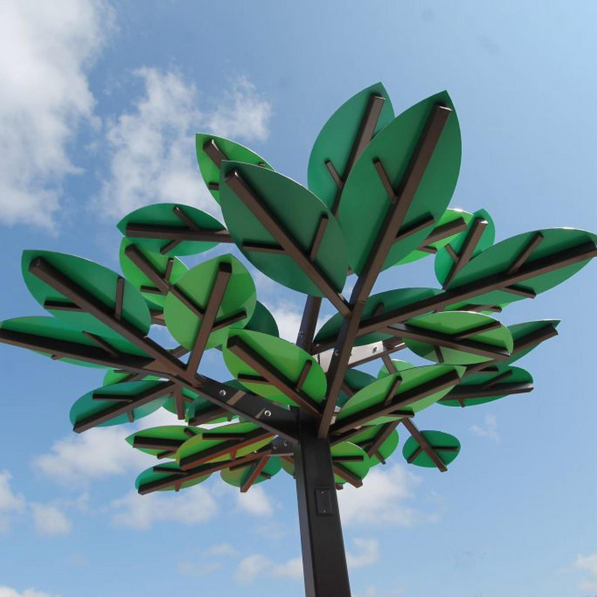 A large metal tree structure with green, geometric leaves made from Heavy Duty Aluminum Composite Material Panel ~ ALPOLIC/HD Series stands against a blue sky with scattered clouds.