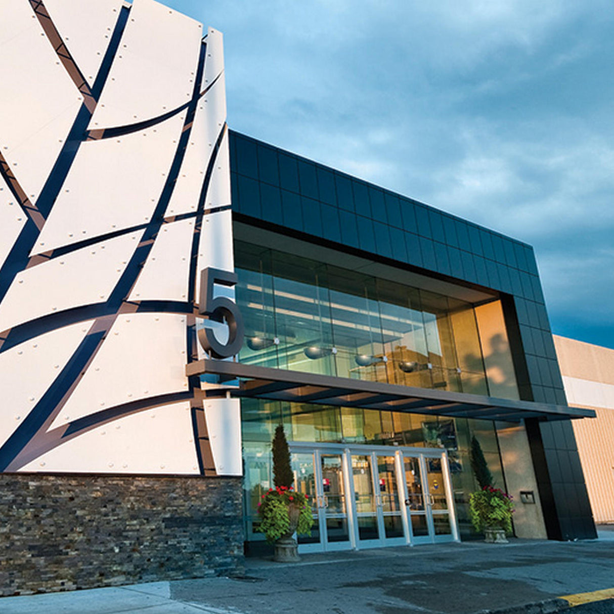 Modern building entrance with large glass doors and a striking black-and-white exterior featuring ALPOLIC/PE Series Lightweight Aluminum Composite Material Panels. The number 5 is prominently displayed, with potted plants by the door under a cloudy sky.