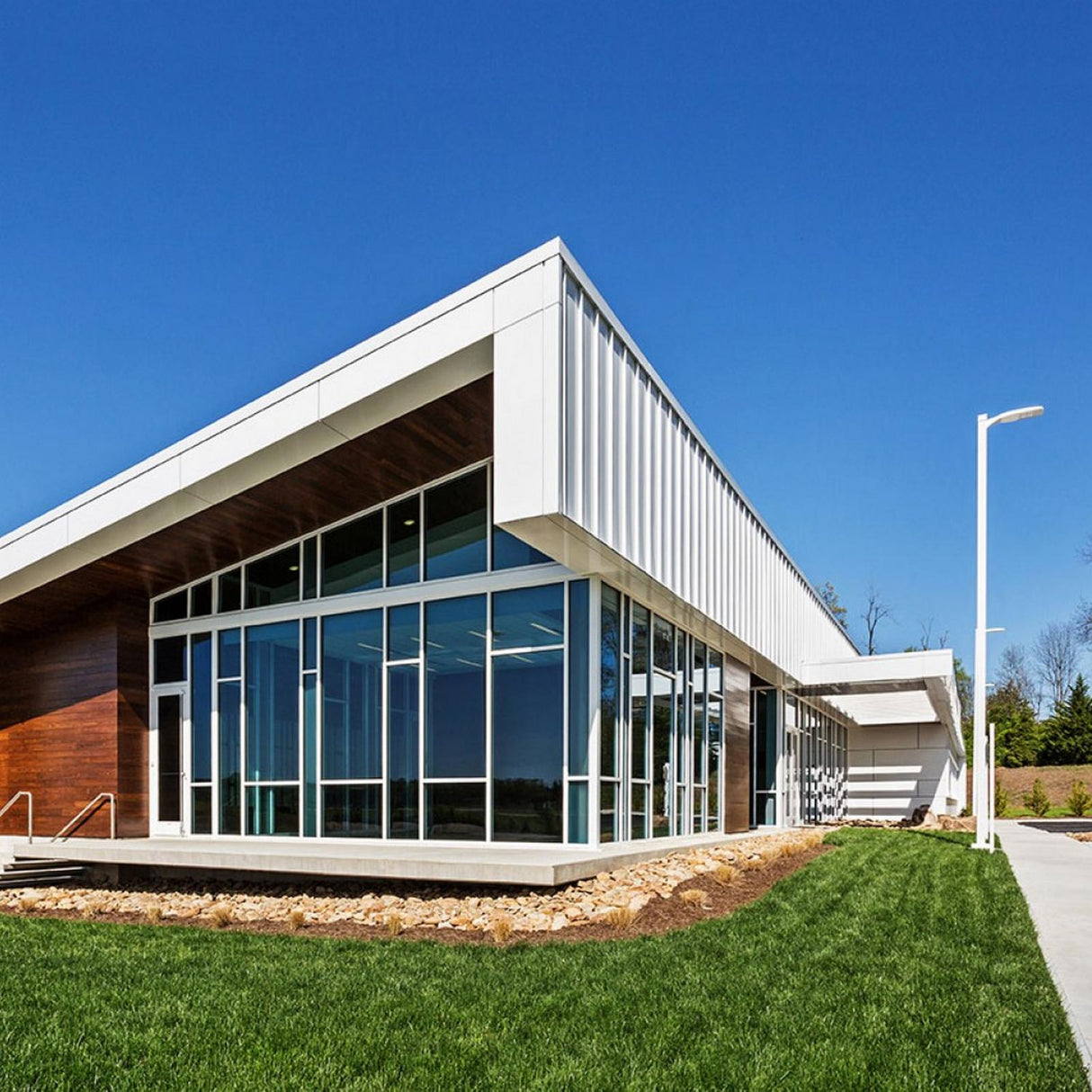 A modern building with large glass windows, a sloped roof, and white ALPOLIC/PE Series lightweight aluminum composite panels for durability, surrounded by green landscaping under a clear blue sky.