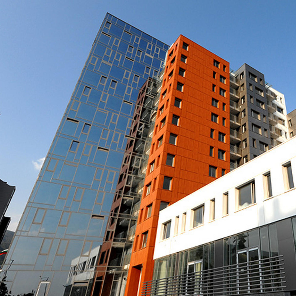 Modern multi-story buildings feature glass, orange, and beige facades with ALPOLIC/RF Series Reflective Aluminum Composite Material Panels, offering striking reflectivity. Geometric designs and large windows highlight contemporary urban architecture under clear blue skies.