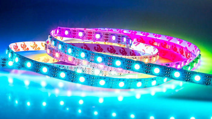The RGB Pixel SK6812 IP20 LED Strip (5V) ~ Lantana Series emits vivid blue, pink, and green hues against a glowing backdrop, highlighting its customizable lighting effects.