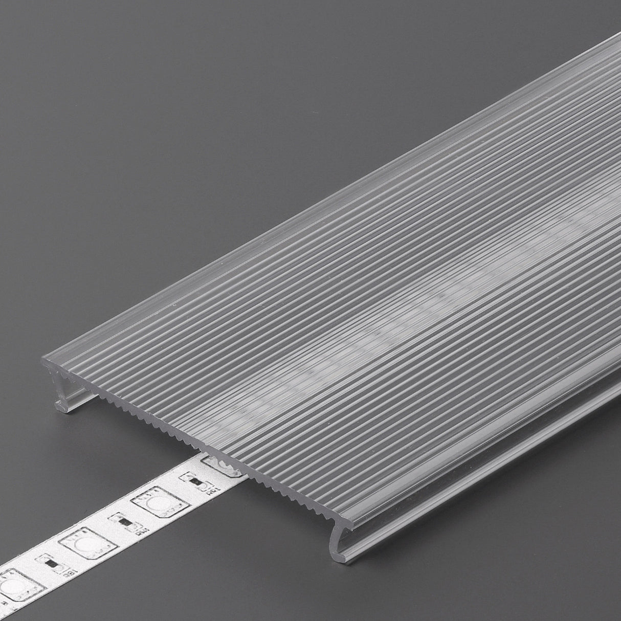The LED Channel Cover ~ C10 Click, a translucent ribbed opal PMMA profile, partly conceals a white LED strip light on a gray surface as a tape measure displays the width.