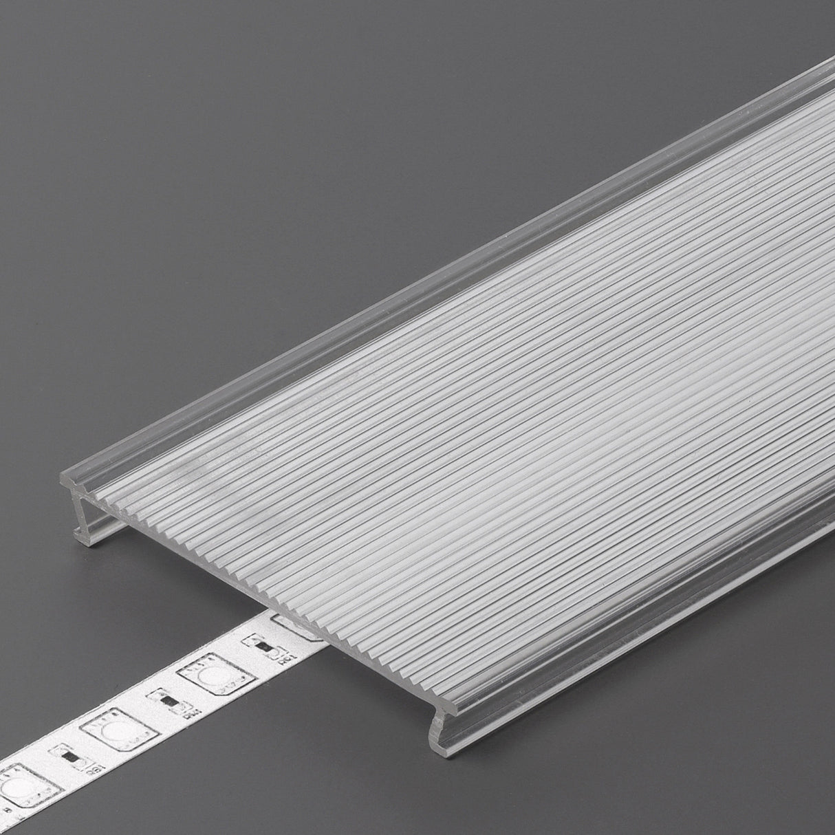A translucent ribbed opal PMMA cover partially conceals a strip of LED lights on a gray surface, highlighting the sleek design of the LED Channel Cover ~ C10 Click.