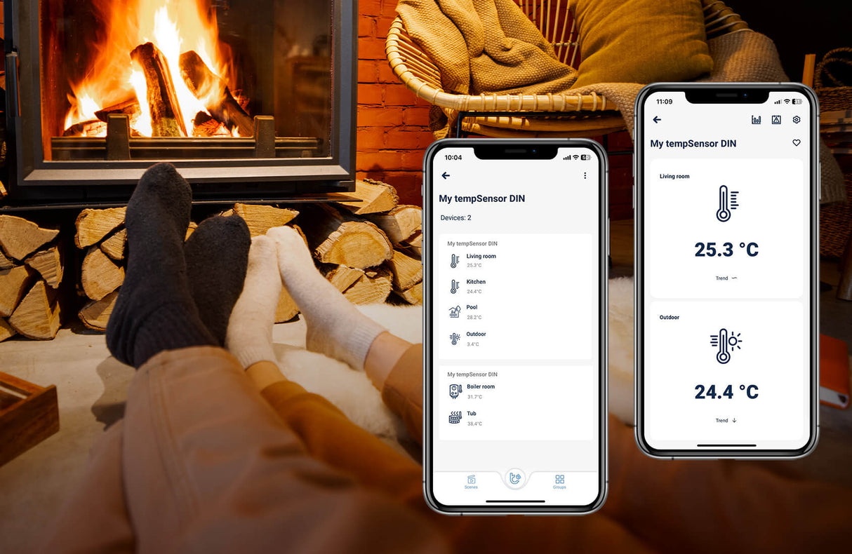 Two people with socks relax by a fireplace, firewood stacked nearby. Two smartphones display the tempSensor DIN by Blebox app for monitoring indoor and outdoor temperatures with the DIN-rail Smart Wireless Temperature Sensor.