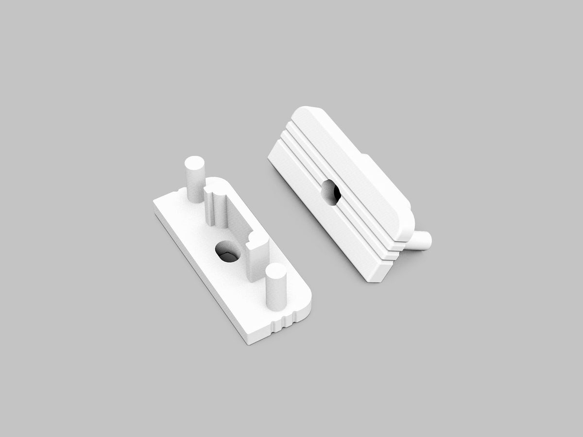Two white plastic End Caps for the Surface10 Profile are shown on a plain gray background. Each component features cylindrical pegs, rectangular bases, geometric cutouts, and raised ridges, indicating they are designed to fit together as LED accessories.