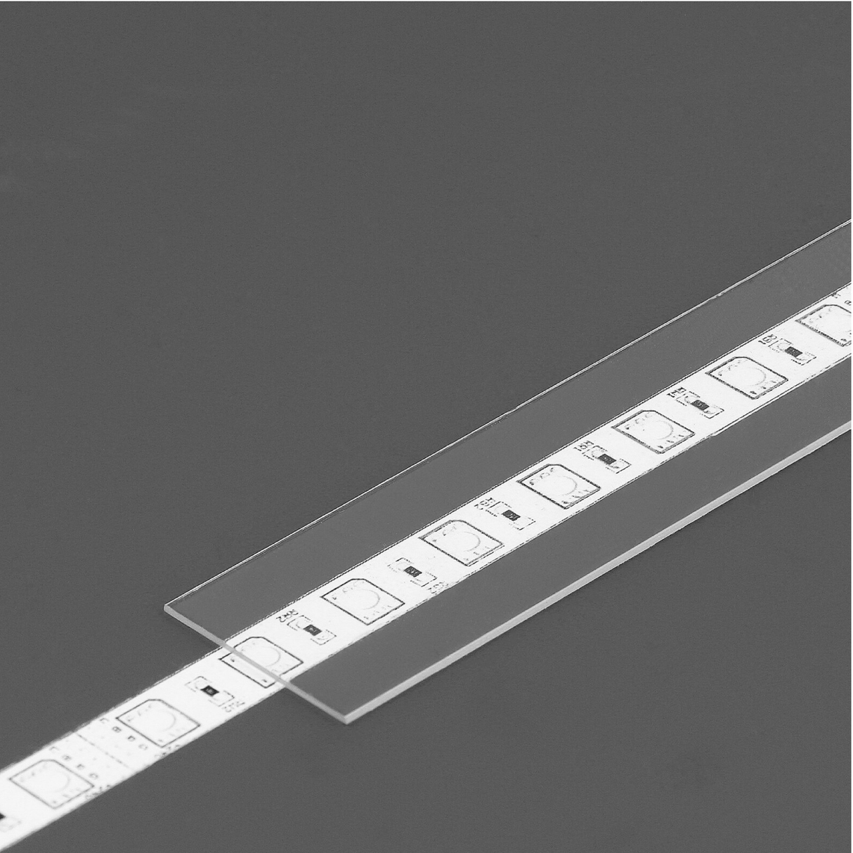 An LED Channel Cover ~ A6 Slide, featuring a white strip with square LEDs, lies on a dark gray surface and is partially covered by its clear slide-in diffuser.