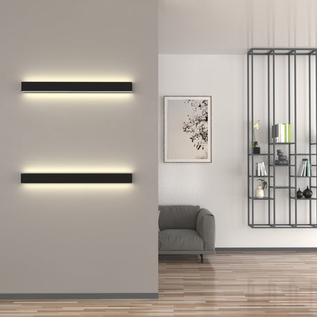 A modern living room featuring the Up & Down Wall Feature Lighting LED Profile ~ Model New Washington, a gray armchair, framed abstract art, and a black metal shelf with decor on a wooden floor.