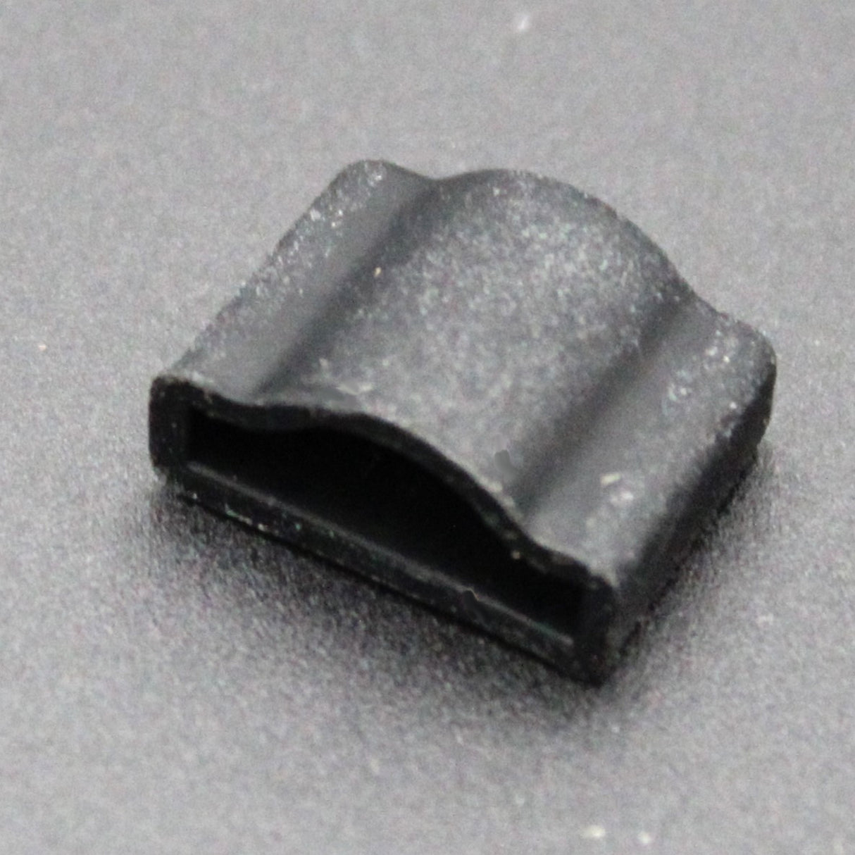 Close-up of the Endcap for Optimum Black Neon Max—a small, black, rectangular plastic clip with a curved top—resting on a dark surface. Ideal for securely attaching neon accessories.