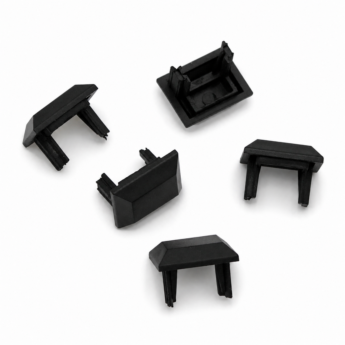 Five small, black plastic Cut & Connect End Caps for Roma Profile, each with prongs and a rectangular shape, are arranged on a white surface. Designed to securely cover the ends of open tubes or rectangular sections, these end caps provide an IP65 seal—ideal for protecting connections in linear lighting systems.