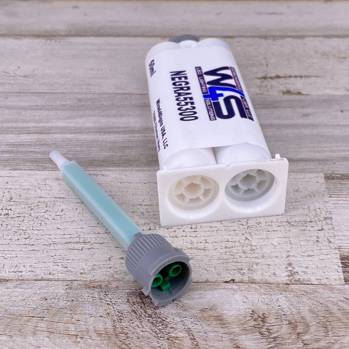 A Black 2-part Methacrylate Adhesive cartridge, W4S 55300 (50ml 1:1 Mix B-System), for structural bonding, rests on a wooden surface next to a green and gray mixing nozzle.
