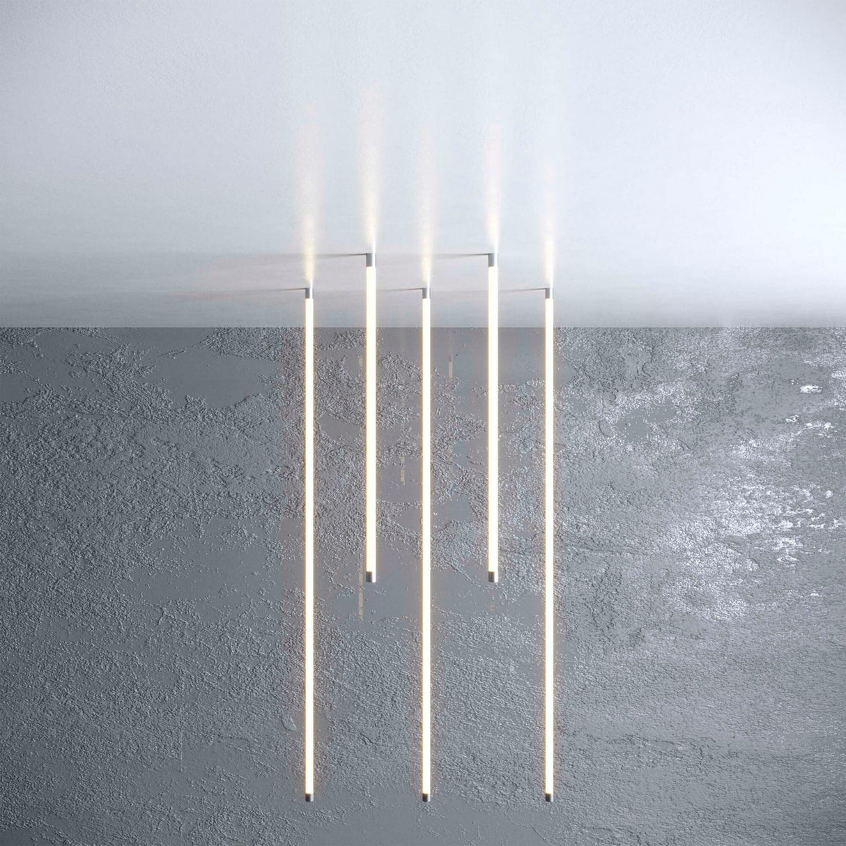 Four Vertical Hanger for Neon 360 Series LED bars hang from a white ceiling with cable suspension kits above a textured gray wall, emitting a soft glow and creating a modern, minimalist aesthetic.