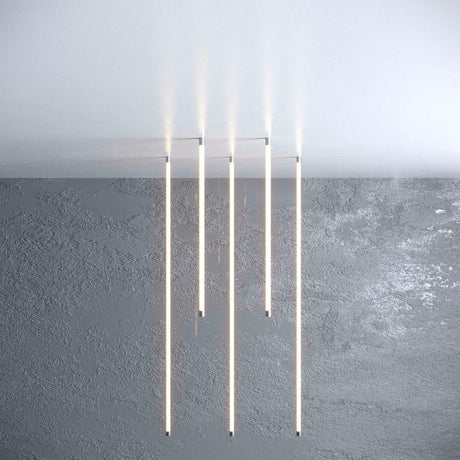 Four Vertical Hanger for Neon 360 Series LED bars hang from a white ceiling with cable suspension kits above a textured gray wall, emitting a soft glow and creating a modern, minimalist aesthetic.