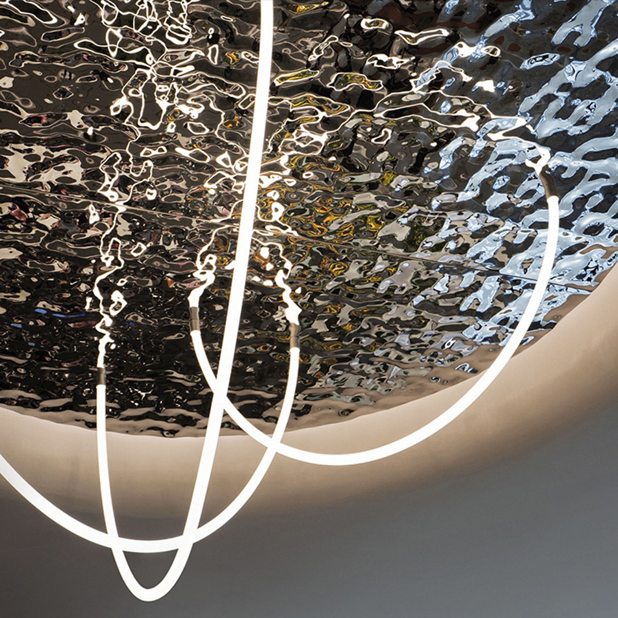 Flexible White LED Neon Tube ~ Neon 360 Series fixtures hang before a rippled, reflective metallic ceiling, producing an abstract, modern look with dynamic 360-degree illumination and striking distorted reflections.