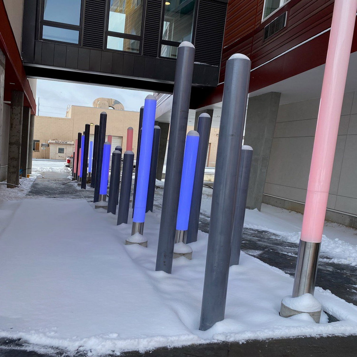 RGBW LED Pillar Tube Light ~ Model Colorado stands upright in two rows on snow-covered ground between modern buildings, creating a vibrant and dynamic outdoor art display that brightens the modern space.