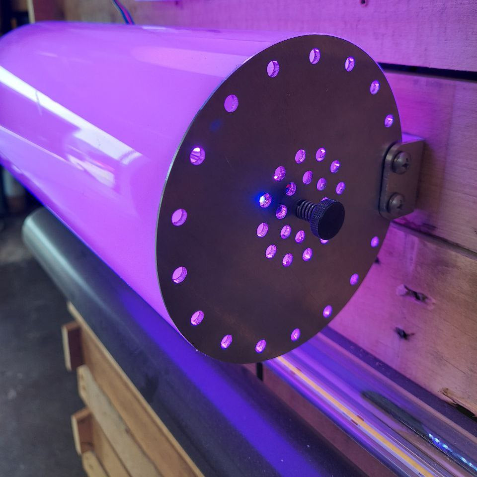 The Surface Mounting Bracket for Large Tube Profiles securely attaches cylindrical devices to wooden walls, featuring a metallic end plate with multiple holes and a central sensor, and emits bright purple light.