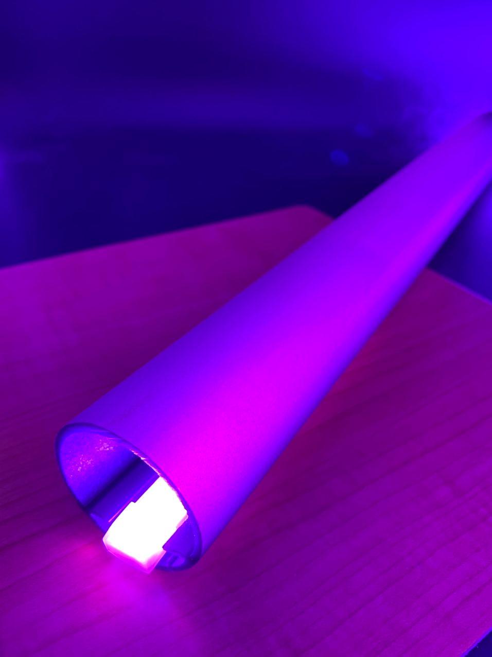 A Bright RGB IP68 LED Strip (24V) ~ Verbena Series, shaped cylindrically and finished in silver, emits vivid purple light from its Osram LEDs as it rests on wood, casting a vibrant glow in the darkness.