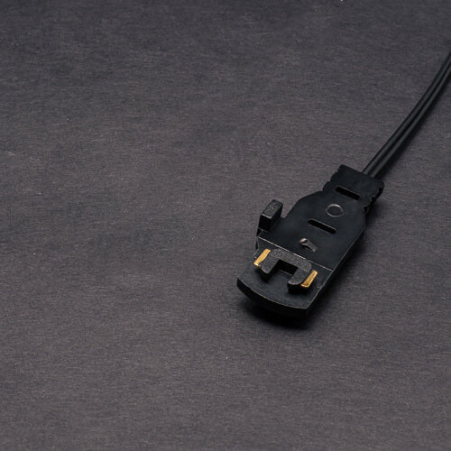 Close-up of a Power Track Twist Plug Connector in black with gold contacts, attached to a cable on a dark gray textured surface—perfect for connecting LED fixtures or integrating with Power Track Twist systems.