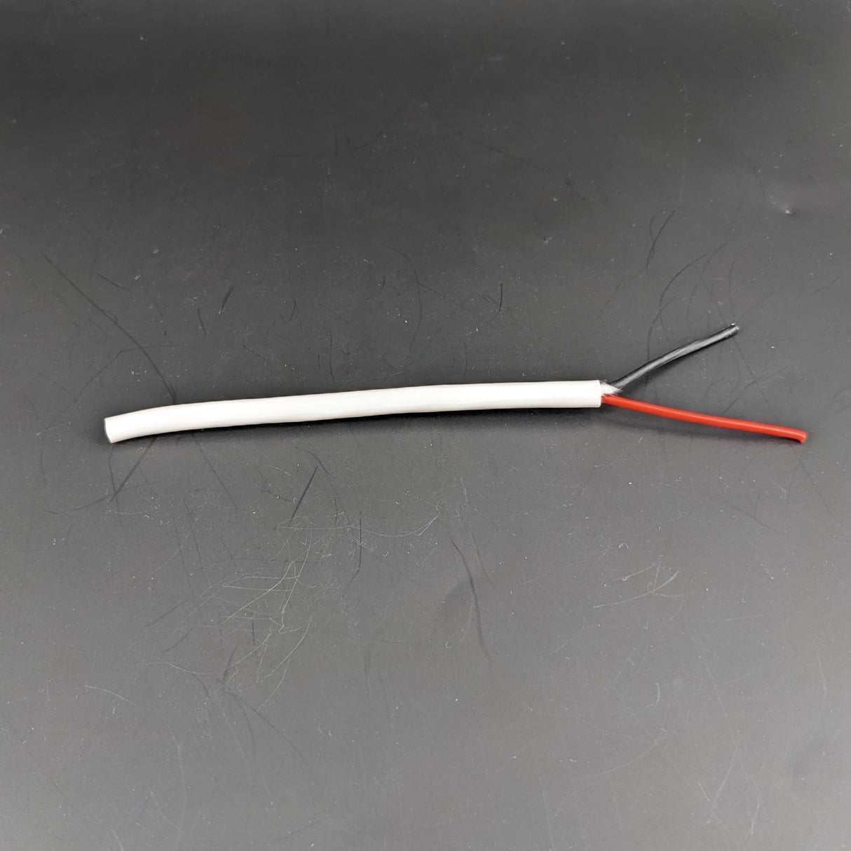 A 2-Core 18 AWG Silicone Electrical Wire, white with stripped ends showing red and black wires, lies on a dark surface.