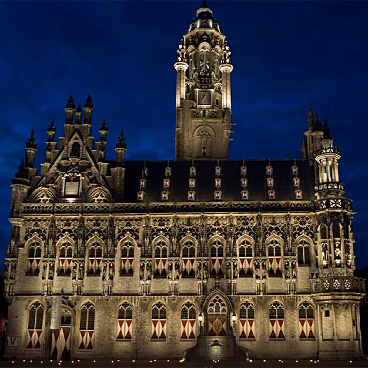 A large, ornate Gothic-style building with decorative spires is illuminated at night by White Outdoor LED Wall Washer Light ~ Revo Basic Magno Dim Series against a dark blue sky.