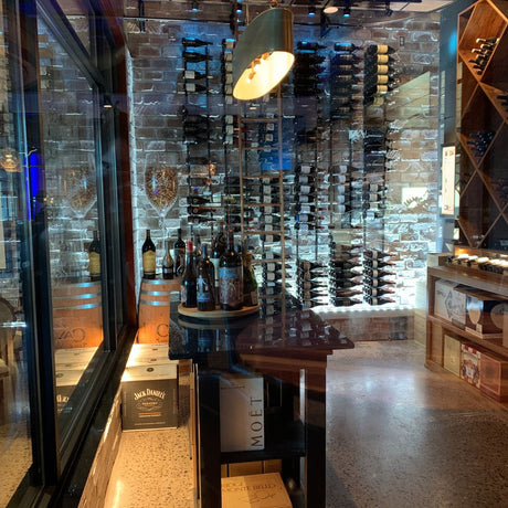 A wine cellar with bottles on wall racks, a table of assorted wines, and wooden boxes; exposed brick walls and cozy lighting from the energy-efficient Slim LED Channel ~ Model Slim8.