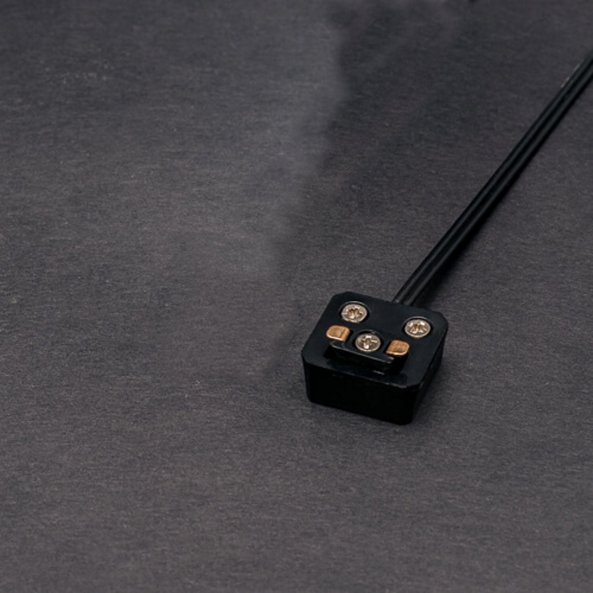 A black Power Track Twist Plug Connector with three visible metal prongs rests on a sleek dark surface, its cable trailing out of the frame—perfect for LED fixture connections.
