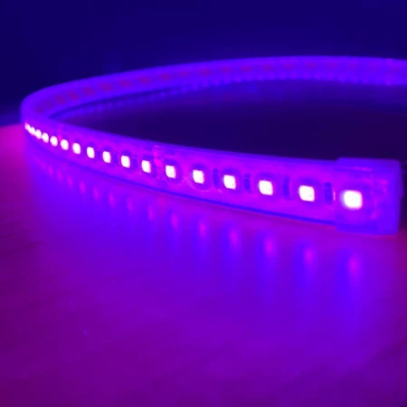 A close-up of the Bright RGB IP68 LED Strip (24V) ~ Verbena Series glowing purple on a wooden surface, with its light reflecting off the floor in a dark setting.