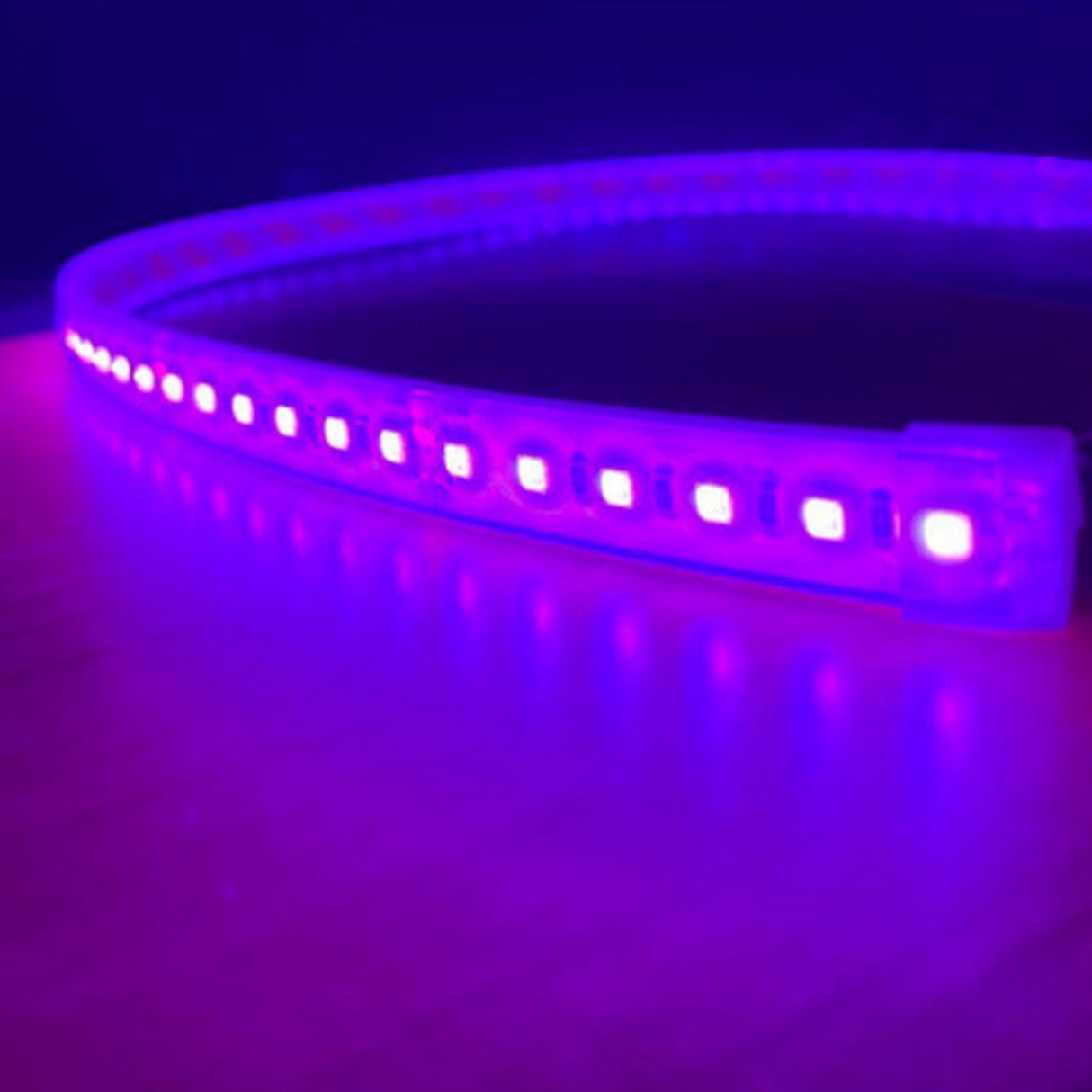 The Bright RGB IP44 LED Strip (12V) ~ Verbena Series glows with vivid purple and pink lights on a wooden surface, casting vibrant reflections.