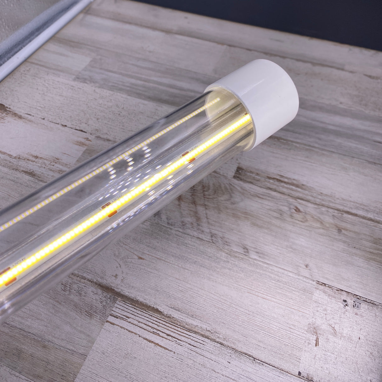 A close-up of an Aluminum End Cover for 1.50 Round Profiles fitted on a clear LED tube light, placed on a light wooden surface, highlighting the product’s sleek and modern design.