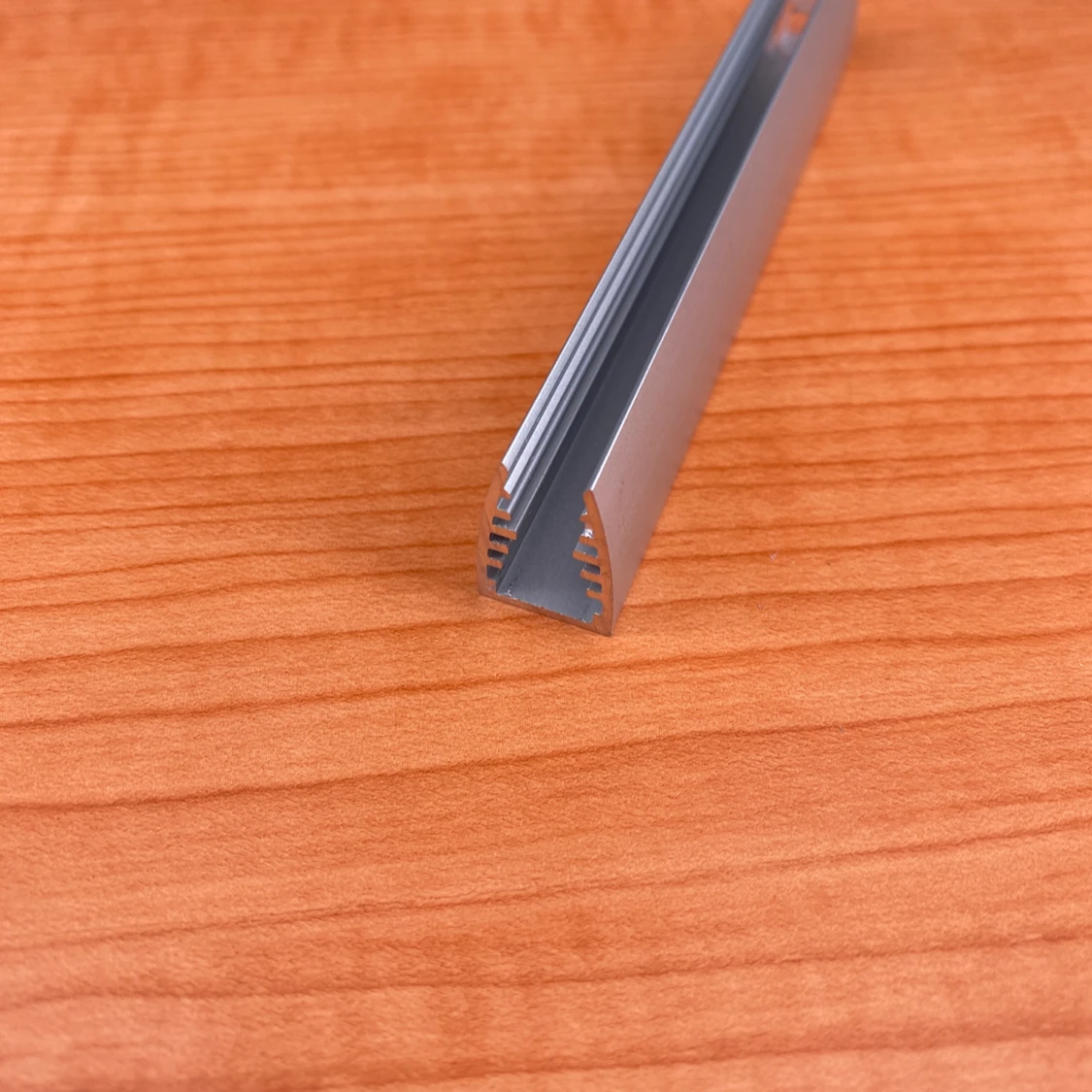 A close-up of the 1/4 LED Edge-lit Acrylic Sign Base Channel ~ Model Mikro10 shows its metallic, U-shaped, grooved design resting on a light brown wood surface.