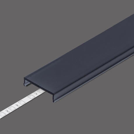 A dark gray LED Channel Cover ~ C7 Click profile cable raceway with a partially inserted strip of adhesive mounting tape is shown on a solid gray background, featuring a clip-in diffuser cover and durable PMMA UV-resistant construction.
