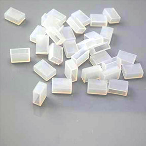 Several small, translucent Waterproof End Cap Covers for IP67/IP68 LED Strips are scattered on a gray surface, perfect for sealing and protecting strip light ends.
