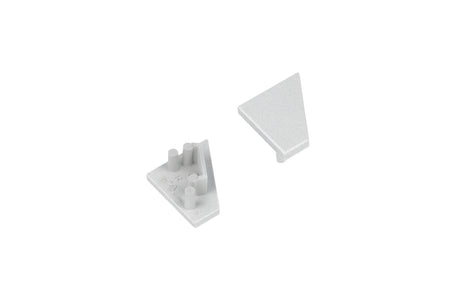 Two small, light gray, triangular plastic End Caps for the Corner10.v2 Profile—one oriented upward to reveal a smooth surface, the other inverted to display pegs and notches on the underside—sit against a white background. These components are designed specifically for use with the Corner10.v2 Profile lighting fixture, providing a clean and secure finish.