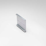 The Mounting Clip for Badalona Profile is a metallic, rectangular aluminum bracket with top and bottom flanges, a smooth finish, and two central screw holes, displayed against a plain light background.