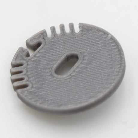 The End Cap for Alu Round Profile is a round, flat, gray plastic cap with a central oval cable hole and four small notches along one edge, designed for Alu Round LED profiles and shown on a white background.