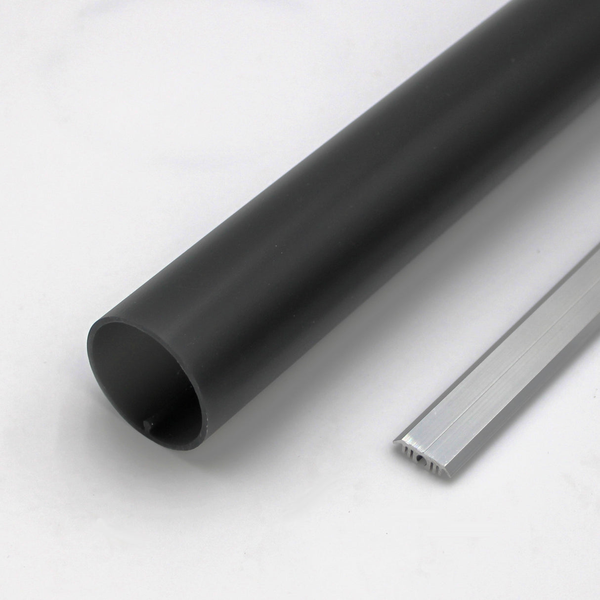 A 1.50 Polycarbonate LED Tube (Model Sierra38) in black and a silver metallic rectangular ridged strip are side by side on a white surface.