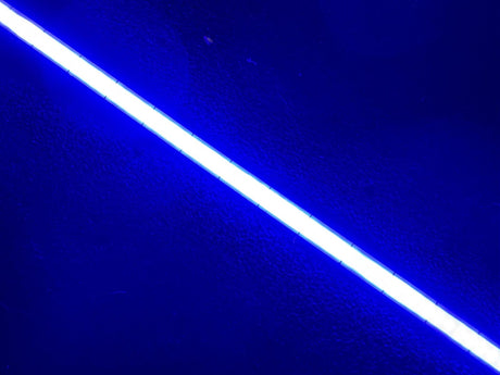 The COB IP20 450nm LED Strip For Medical Lighting (5V) ~ Aloe Vera Series emits a vibrant white glow, illuminating a textured dark blue background.