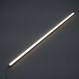 The White Universal Surface-mount LED Lighting Fixture ~ Begton12 Series, a long, slim fixture, emits a bright, dotless white glow and is placed diagonally against a dark background.