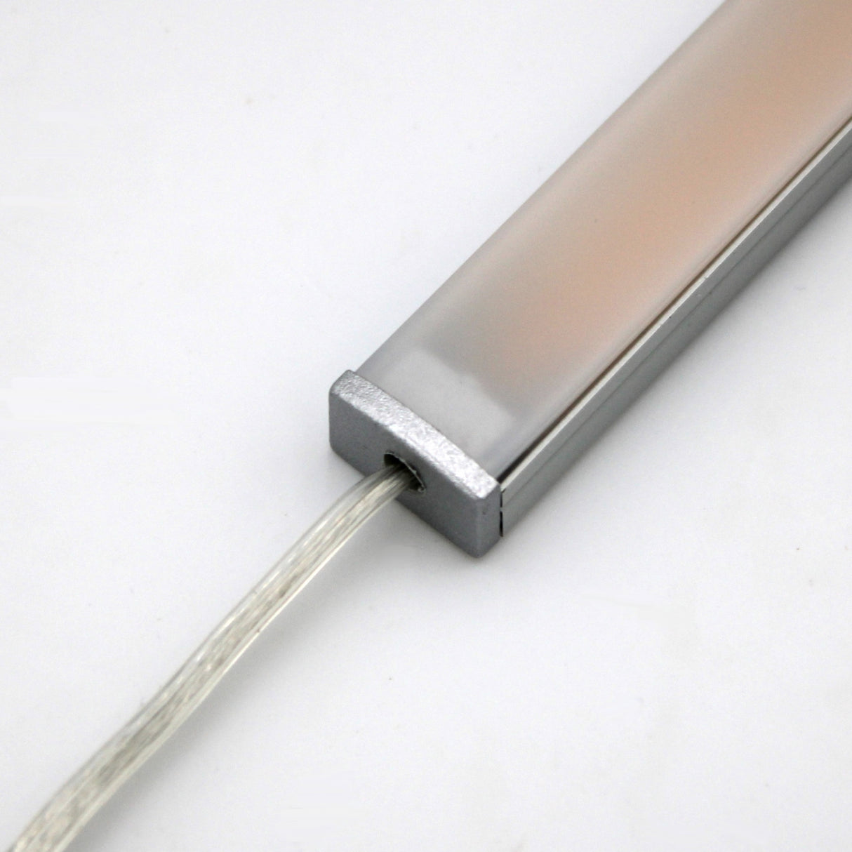 A close-up of the White Universal Surface-mount LED Lighting Fixture ~ Begton12 Series features a rectangular, dotless design with a frosted cover, metallic end cap, and transparent power cord against a plain white background.