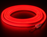 The Color IP44/IP66 Neon Flexible LED Light Line (24V) ~ Flex Ultra Slim Series emits a vibrant red glow while coiled, standing out against a dark backdrop, with two exposed wires visible at one end.